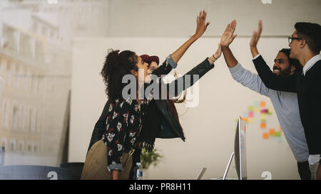 Colleghi di lavoro dando alta cinque per ogni altro in piedi in ufficio. I membri del team per celebrare il successo sul lavoro dando alta 5. Foto Stock