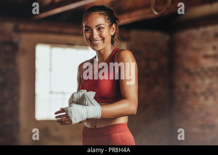 Pugile donna con cinturino al polso per allenarsi con la boxe. fitness donna che si prepara per gli allenamenti di boxe. Bella giovane donna con corpo muscolare pre Foto Stock