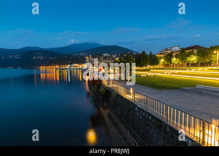 Lago al tramonto. Il Lago Maggiore e la città turistica di Luino con il suo bellissimo lungolago illuminata su una bella serata estiva Foto Stock