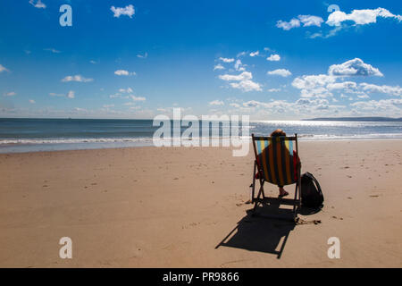 Un lone persona gode della solitudine, seduto in una sedia a sdraio con una spiaggia tutta per se stessa - nessuno lì, solo la possibilità di sedersi e di sogno Foto Stock