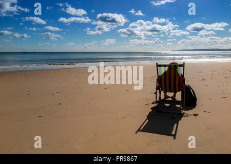 Un lone persona gode della solitudine, seduto in una sedia a sdraio con una spiaggia tutta per se stessa - nessuno lì, solo la possibilità di sedersi e di sogno Foto Stock