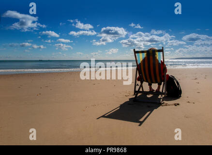 Un lone persona gode della solitudine, seduto in una sedia a sdraio con una spiaggia tutta per se stessa - nessuno lì, solo la possibilità di sedersi e di sogno Foto Stock
