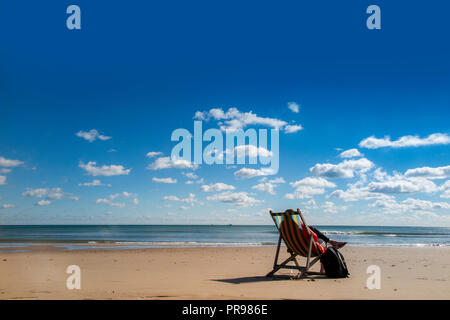 Un lone persona gode della solitudine, seduto in una sedia a sdraio con una spiaggia tutta per se stessa - nessuno lì, solo la possibilità di sedersi e di sogno Foto Stock