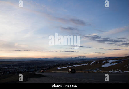 Si affaccia sulla città di Cochrane in un tramonto in inverno con fabbriche per la cottura a vapore contro le montagne rocciose. Foto Stock