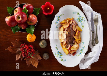 Arrosto di filetto di maiale con le mele sulla piastra bianca, tipica per l'autunno-inverno ricetta. Fotografato dal di sopra. Foto Stock