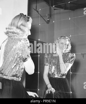 Make-up nel 1940s. Una giovane donna bionda ad una festa sta in piedi davanti ad una parete dello specchio, che la migliora. Indossa una blusa glittery con un retro alla moda aperto visibile. Svezia 1943. Foto Kristoffersson C122-3 Foto Stock