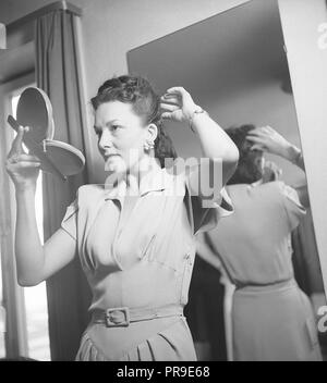Donna che fissa i capelli negli anni '1940s. Una giovane donna dai capelli scuri si sta guardando in uno specchio da tasca mentre fissa i suoi capelli. Svezia 1947. Foto Kristoffersson Ref U118-2 Foto Stock