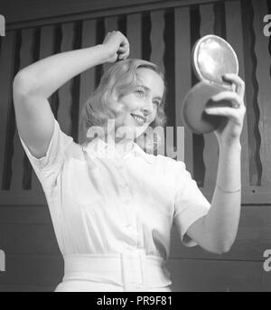 Donna che fissa i suoi capelli nel 1940s. Una giovane donna bionda sta guardando a se stessa in un specchio tascabile mentre pettinare i capelli. La Svezia 1943. Foto Kristoffersson ref F7-4 Foto Stock