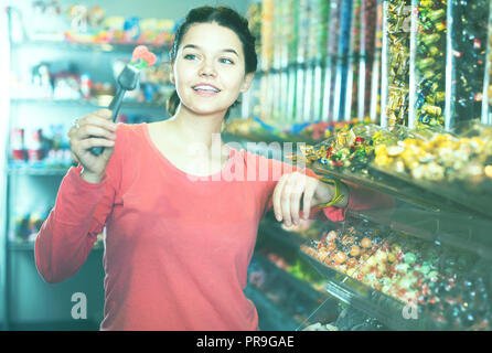 La ragazza è felice di prendere in considerazione i diversi tipi di caramelle in negozio Foto Stock