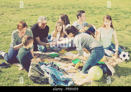 Sorridente famiglia con i bambini a parlare e mangiare la pizza a picnic nel parco Foto Stock