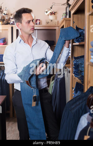 Maschio adulto cliente esaminando i pantaloni in panni maschio store Foto Stock