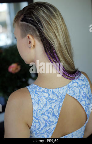 Thin pigtail capolino da sotto i capelli delle ragazze, viola trecce di capelli stile giovanile, close-up di una ragazza su uno sfondo di fiori Foto Stock