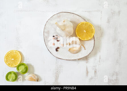 Organici bulbo aglio e chiodi di garofano visualizzato sul legno bianco con fetta di limone, i pomodori verdi e sale himalayano. Vista superiore Foto Stock