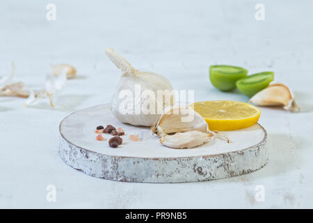 Organici bulbo aglio e chiodi di garofano visualizzato sul legno bianco con fetta di limone, i pomodori verdi e sale himalayano. Foto Stock