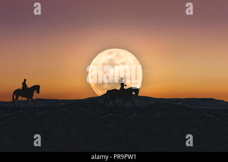 Silhouette di un uomo e di una donna a cavallo tra orizzonte mentre il Full Moon Rising Foto Stock