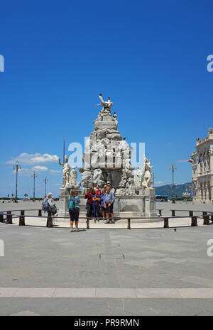 I turisti in piedi dalla fontana (Fontana dei Quattro continenti) in Piazza Unita d'Italia, Trieste, Italia, mentre un altro turista prende le loro foto. Foto Stock