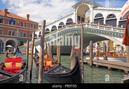 Due gondole ormeggiate nella parte anteriore del ponte di Rialto di Venezia, Italia. Immagine mostra i turisti sul ponte, con una barca a motore ormeggiata nei pressi di gondole e l'uomo nelle vicinanze. Foto Stock