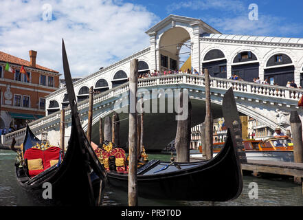 Due gondole ormeggiate nella parte anteriore del ponte di Rialto di Venezia, Italia. Immagine mostra i turisti sul ponte e imbarcazione a motore ormeggiate vicino gondole. Si tratta di una giornata di sole. Foto Stock