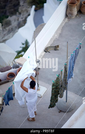 Signora appeso fuori bianco appesi per asciugare in aria Oia landmark cupola blu chiese SANTORINI, CICLADI un gruppo di isole in Grecia, turisti salire a piedi a t Foto Stock