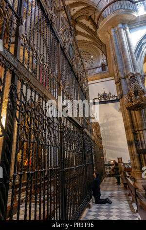 L'uomo sulle ginocchia pregando davanti della cancellata in ferro battuto decorato con disegni e scudi con un gotico rinascimentale design, il Monastero reale di Guadalupe Foto Stock