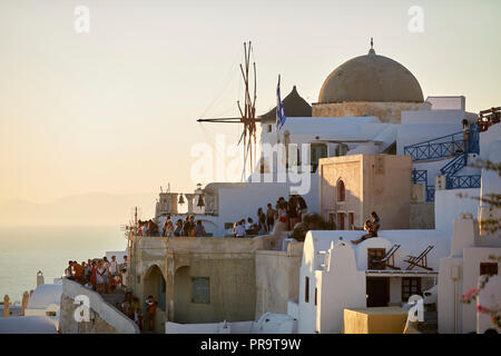 Tradizionale della scogliera case laterale di Oia landmark mulini a vento SANTORINI, CICLADI un gruppo di isole in Grecia, i turisti a piedi fino alla ripida collina Foto Stock