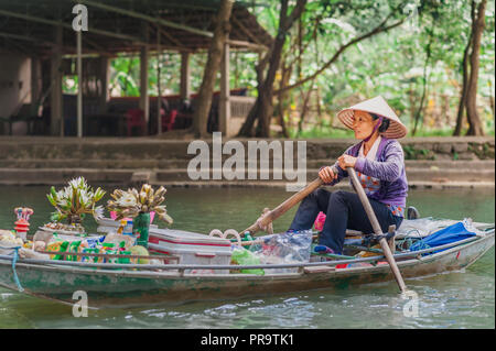 Ottobre 17, 2016 - Van Lam Village, Vietnam. Donna locale in un riso hat remare una barca con merci per la vendita lontano dal Vung Tram Pier. Foto Stock