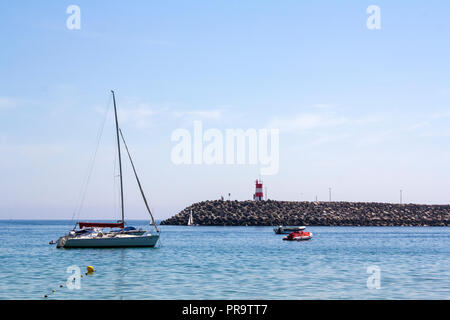 Barche in mare e pier con faro rosso Foto Stock