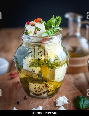 Close-up di marinata di formaggio feta in olio d'oliva, erbe e peperoncino rosso su sfondo di legno Foto Stock