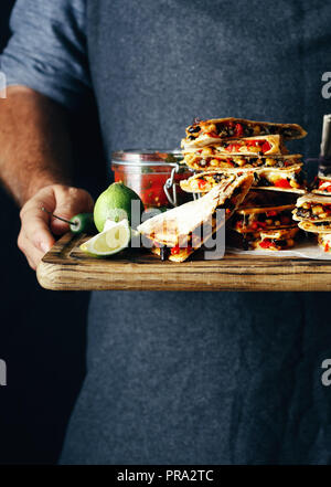 L'uomo detiene sul tagliere snack per la birra: quesadilla con verdure e formaggio con birra chiara Foto Stock