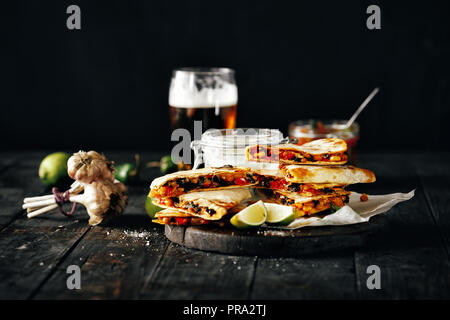 Snack per la birra scura sul tavolo di legno: quesadilla con verdure e formaggio con birra chiara su sfondo scuro Foto Stock