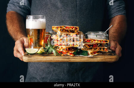 L'uomo detiene sul tagliere snack per la birra: quesadilla con verdure e formaggio con birra chiara Foto Stock