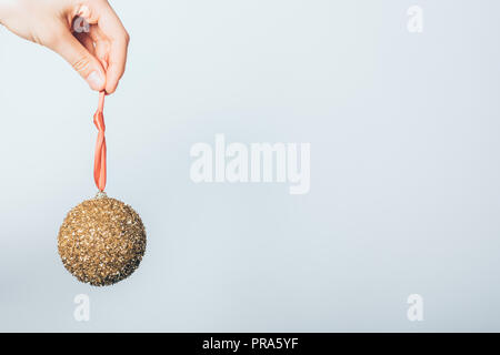 Close-up di donna di mano azienda nuovo anno palla dorata appesa al nastro rosso. Albero di natale decorazione giocattolo su sfondo bianco con copia spazio. Foto Stock