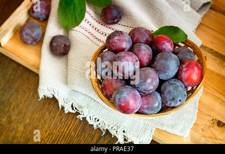 Sul tavolo su un tovagliolo cesto in vimini riempito con maturi grandi prugne. Foto Stock