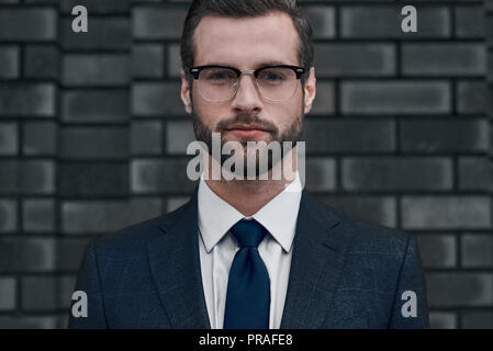 Un fiducioso vista del leader. Un giovane imprenditore in bicchieri e con una barba guarda direttamente a voi Foto Stock