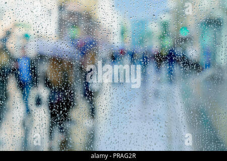 Gocce di pioggia sulla finestra bagnata, offuscata la gente, city light bokeh di fondo. Concetto di tempo piovoso, stagioni, città moderna. Copia dello spazio, per sfondo astratto Foto Stock