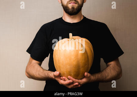 Giovane uomo barbuto in black t-shirt azienda grande zucca nella parte anteriore del petto Foto Stock