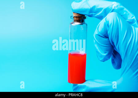 Una mano tiene una provetta di liquido rosso su sfondo blu. La ricerca medica in laboratorio. Foto Stock