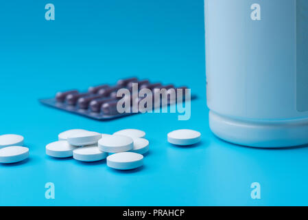 Le pillole bianche sparse su uno sfondo blu e una bottiglia aperta. Vista ravvicinata, farmaci. Foto Stock