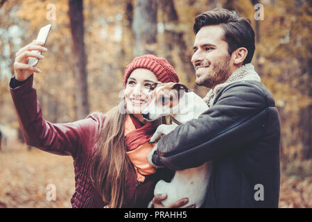 Donna e uomo con il loro cane in autunno a piedi prendendo un telefono selfie Foto Stock