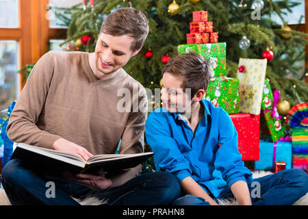 Il Daddy la lettura dal libro per bambini sotto X-mas tree Foto Stock