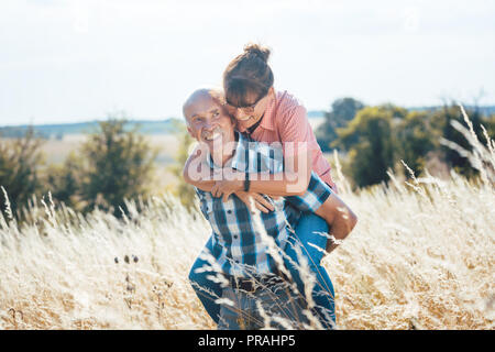 Senior uomo portando la sua moglie piggyback sulla sua schiena Foto Stock