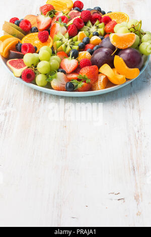 Una sana frutta, fragole lamponi arance Prugne Mele Kiwi uve, mirtilli bianco sul tavolo di legno, verticale, spazio di copia Foto Stock