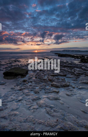 Compton Bay, Isle of Wight, Regno Unito. Il 30 settembre, 2018. Un bellissimo e suggestivo tramonto sulla spiaggia e rocce di Compton bay sull'Isola di Wight. Lo scambiatore di calore autunno Meteo portando un cielo nuvoloso e Moody per sentire il mare e le scogliere con la bassa marea. I colori del tramonto riflesso sul bagnato di sabbia e alghe marine rocce coperte. Credito: Steve Hawkins Fotografia/Alamy Live News Foto Stock