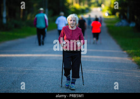 Donna anziana impegnata in Nordic walking con bastoni. Foto Stock