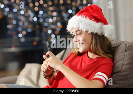 Felice adolescente invio di messaggi in natale seduto su un divano nel salotto di casa Foto Stock