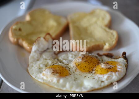 Uova fritte, Sunny Side, sulla piastra con pane imburrato. Foto Stock