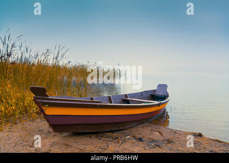 La barca di legno sulla riva del lago. Autunno foschia mattutina a thew lago Foto Stock