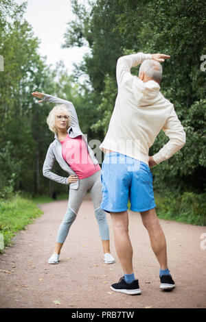 Attivo Coppia matura in sportswear fare esercizio fisico nel parco, tra il verde degli alberi Foto Stock