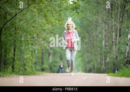 Active donna matura in sportswear lungo la strada nel parco con alberi verdi intorno Foto Stock