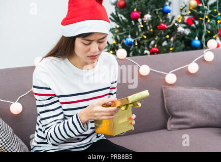 Donna asiatica sconvolto quando apri oro xmas confezione regalo a festa sul divano,noia Christmas party presente Foto Stock